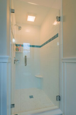 Une douche fermée par des parois en verre, avec des carreaux blancs et une petite étagère.
