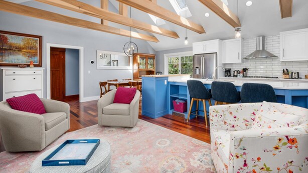 A spacious living area with a dining table, sofas, and a kitchen with white cabinets and a blue island.