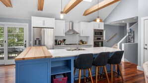 A modern kitchen with white cabinets, a marble island, and a wooden ceiling.