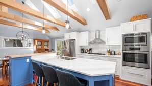 A modern kitchen with white cabinets, a large island with bar stools, stainless steel appliances, and a skylight.