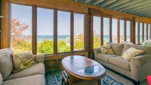 Una habitación con un ventanal grande con vista al mar, techo de madera y un sofá beige con cojines.