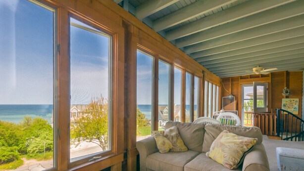Una habitación con un amplio ventanal con vistas al océano, un sofá color beige con cojines y un ventilador de techo.