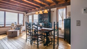 A wooden-floored dining area with a table and chairs, a chandelier, and a view of the sea through large windows. - Modern Post & Beam with Stunning Bay Views (Sandwich)