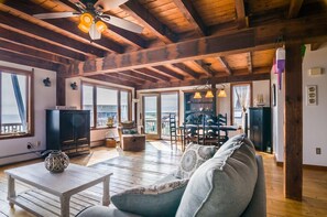 A spacious living area with a wooden ceiling, large windows, a ceiling fan, and a view of the sea. - Modern Post & Beam with Stunning Bay Views (Sandwich)