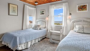 Un dormitorio con dos camas individuales, techo de madera, paredes blancas y vista al mar.