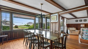 Un comedor amplio con una gran mesa de madera y sillas, ventanas grandes que ofrecen vistas al exterior, y una zona de estar acogedora con un sofá y sillones.