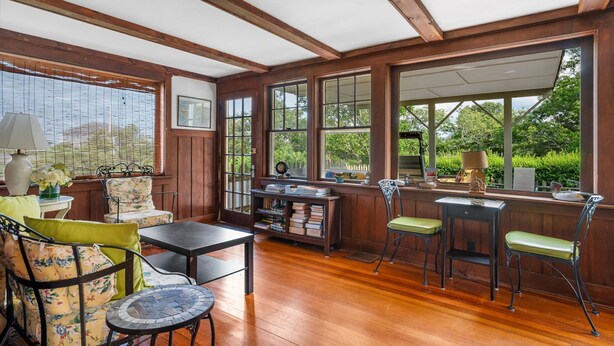 Un rincón acogedor para leer con vigas de madera, ventanas amplias y una mesa de madera con sillas.