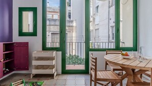 A room with a balcony, a dining table with chairs, a small play area with a toy train set, and a window with a view of buildings. - AMAZING Gran de Gràcia (08012 Barcelona)