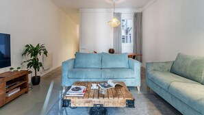A living room with a blue sofa, a coffee table with books, a TV, and a plant. - AMAZING Gran de Gràcia (08012 Barcelona)