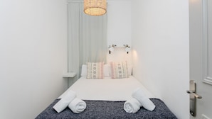 A hotel room with a bed, two pillows, a bedside table, a hanging light fixture, and a door.