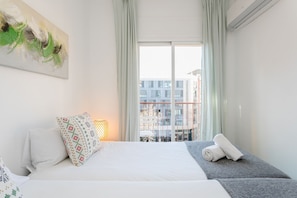 Quarto de hotel com cama, duas almofadas, mesa de cabeceira, luminária e janela com cortinas.