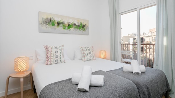 A hotel room with a large bed, two bedside tables, a painting on the wall, and a view of buildings through the window.