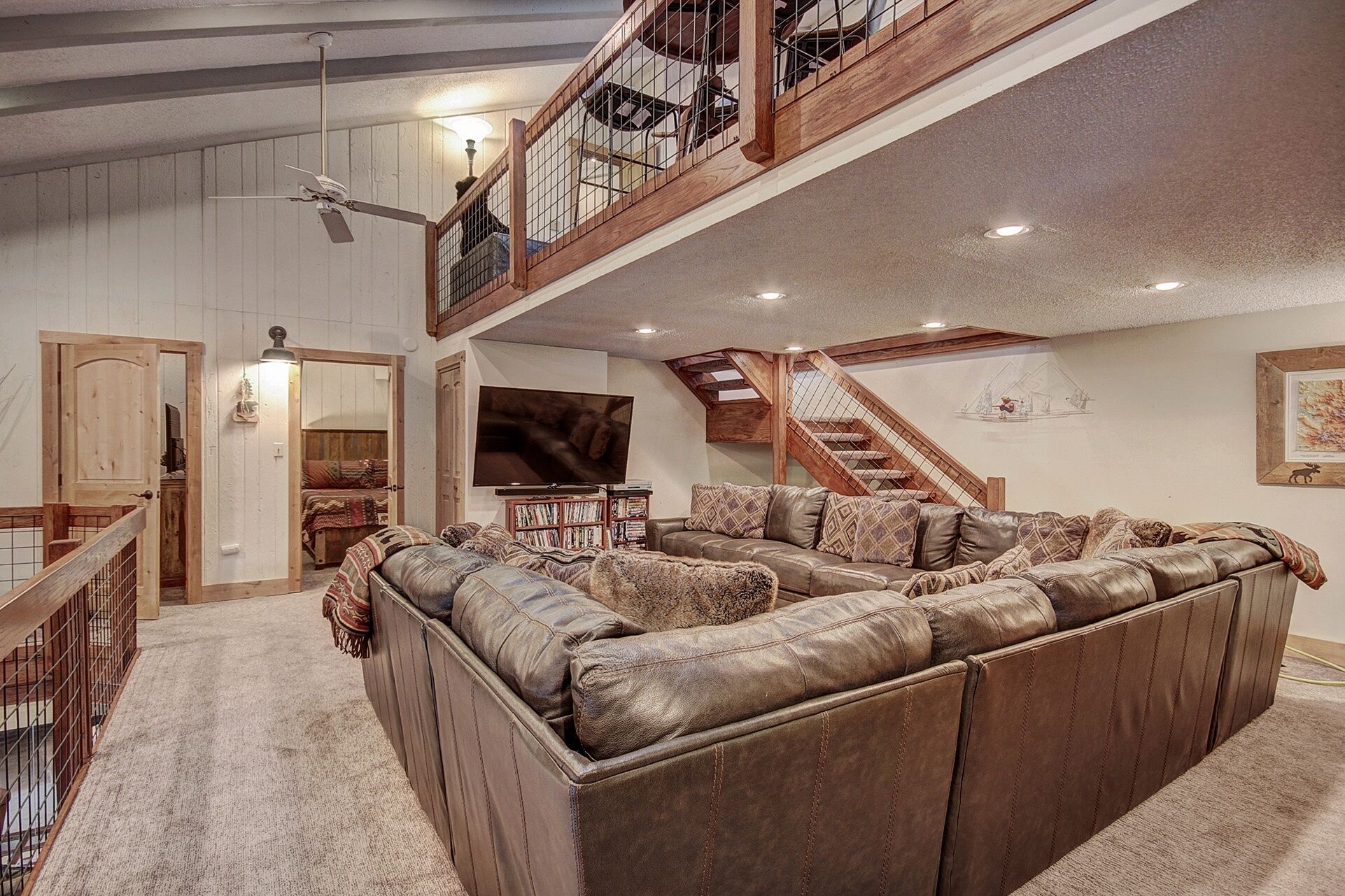 A spacious living room with a large leather sectional sofa, a television, and a staircase leading to an upper level.