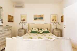 Quarto com cama, duas mesas de cabeceira, cômoda e quadros nas paredes.