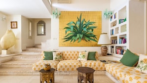 A living room with a sofa set, a large plant painting, a bookshelf, and a staircase. - 2457 Villa Allegra by Perle di Puglia (Castrignano del Capo)