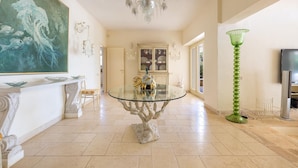 A spacious room with a round glass table, a chandelier, a green floor lamp, and a large painting on the wall. - 2457 Villa Allegra by Perle di Puglia (Castrignano del Capo)