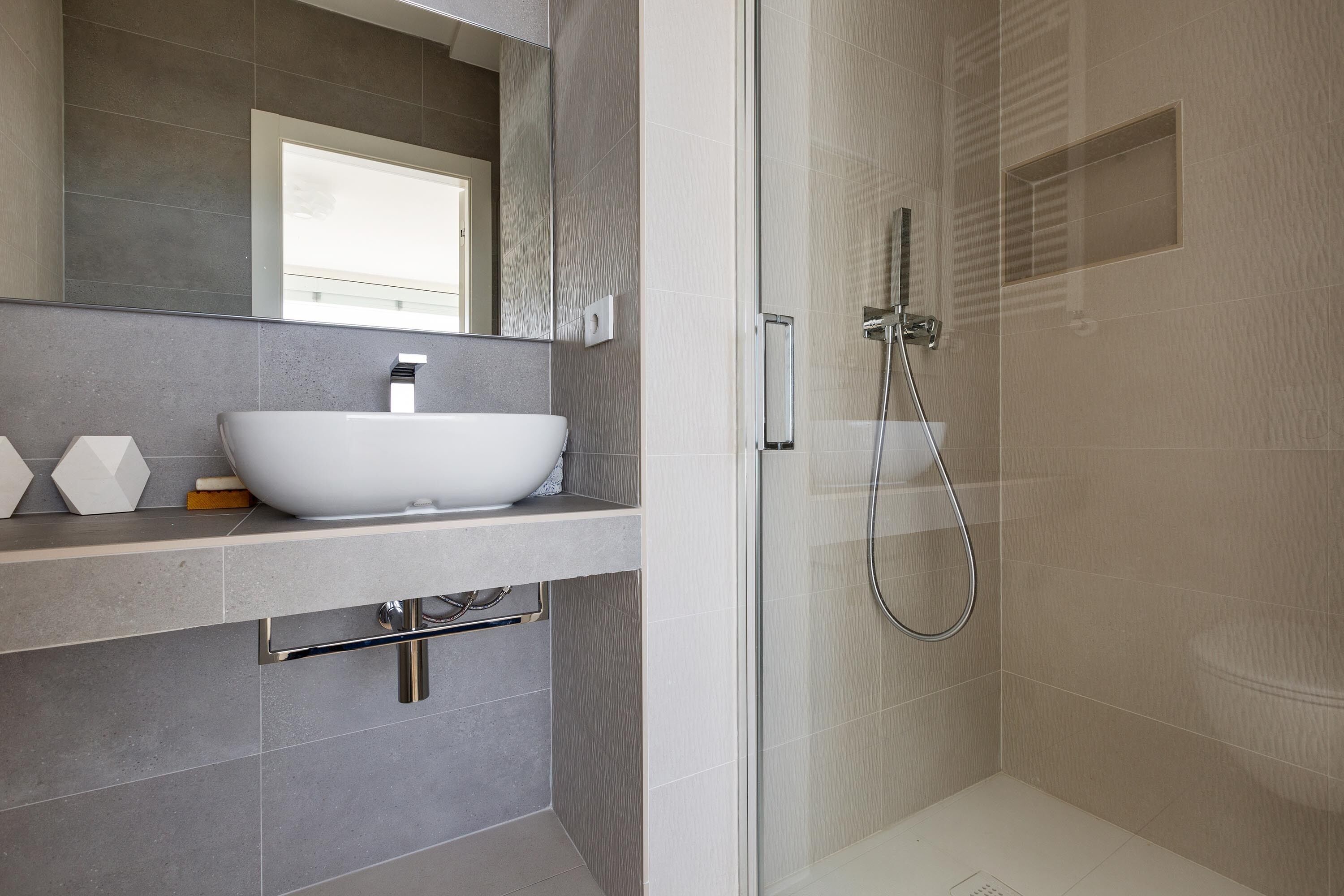 Une salle de bain moderne avec un grand lavabo blanc, une douche à parois de verre et un miroir au-dessus du lavabo.