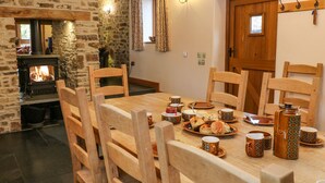 Un rincón comedor acogedor con chimenea de piedra, sillas de madera y una mesa de madera dispuesta con platos, tazas y un hervidor.
