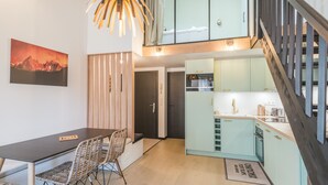 A modern kitchen with light blue cabinets, a wooden dining table with wicker chairs, and a hanging light fixture.