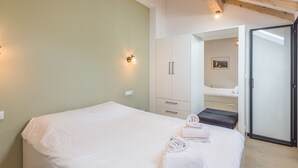 A bedroom with a bed, a wardrobe, a bathroom mirror, and a door leading to another room.