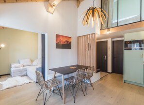 A modern kitchen with a dining area, featuring a wooden table, wicker chairs, and a hanging light fixture.