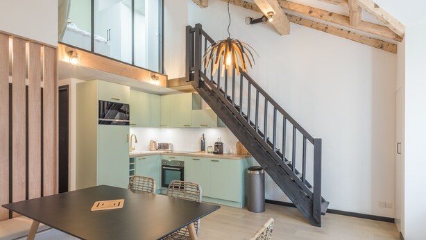 A modern kitchen with a staircase, wooden beams, and a dining area with a table and chairs.