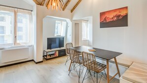A modern living room with a wooden ceiling, a dining table with chairs, a TV, and a mountain painting on the wall.