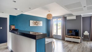 Un salon moderne avec un mur d’accent bleu, un îlot central, un téléviseur à écran plat et un coin repas.