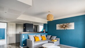 Un salon moderne avec un canapé gris, deux tables basses blanches et un mur d’accent bleu.