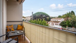 Un balcon avec une table et des chaises, un canapé avec des coussins et une vue sur les bâtiments et les arbres.