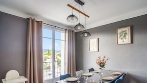 Un coin repas avec une table dressée pour six personnes, une chaise haute et une vue sur l’extérieur grâce à une grande fenêtre.