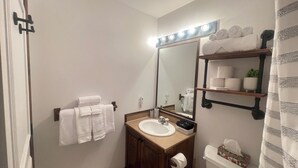 Un baño con lavamanos, espejo, toallero y repisas con artículos de aseo.