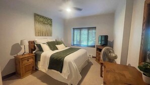 Un dormitorio con cama, mesita de noche, lámpara, ventana con persianas, ventilador de techo y televisor.