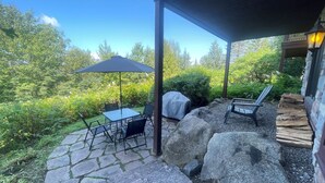 Un patio techado con suelo de piedra, una mesa con sillas, una parrilla y un banco de madera.