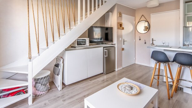 Een ruimtelijk ingerichte leefruimte met een keuken, een eethoek met twee stoelen, een witte tafel en een trap met een touwbalustrade.