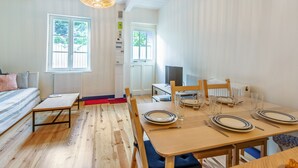 A room with a dining table set for four, a bed with a striped pillow, a wooden floor, and a ceiling with exposed beams.
