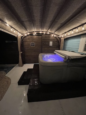 Un jacuzzi con luz azul, rodeado por una terraza de madera y un pequeño banco negro.