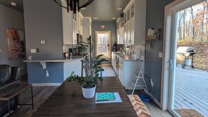 Een moderne keuken met een lange houten tafel, een hangende lamp en uitzicht op de omgeving door een schuifdeur.