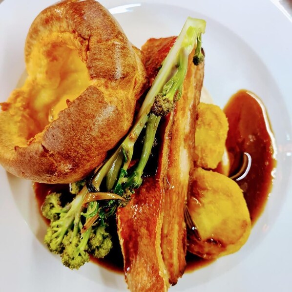 A plate of food with Yorkshire pudding, broccoli, and a piece of meat, possibly pork, with gravy. - 1-bed Apartment in Helston - Resturant and Golf (Helston)