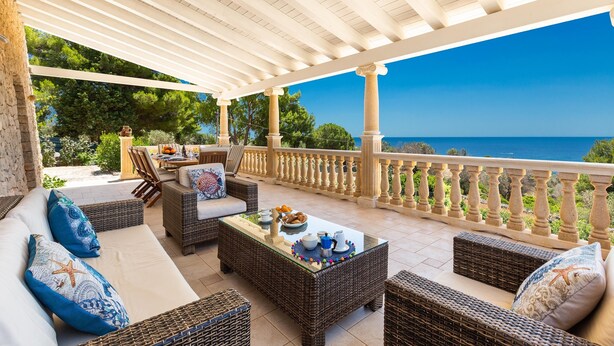 Un espace extérieur aménagé, abrité et doté de mobilier en osier, d’une table basse en verre et offrant une vue sur la mer.