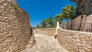 Un chemin de pierres mène à un bâtiment dont un côté est bordé d’un mur de pierres et l’autre d’une clôture.