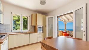 Une cuisine avec vue sur la mer, une table à manger et un pouf rouge.