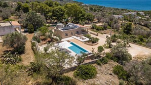 Une grande maison avec une piscine, entourée d’arbres et offrant une vue sur la mer.