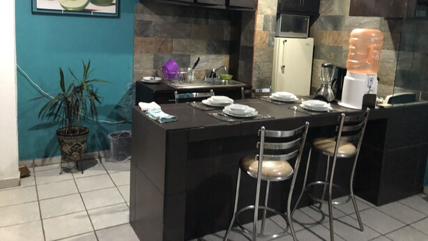A kitchen with a central island, dark cabinets, a refrigerator, a water dispenser, and a potted plant. - BEAUTIFUL APARTMENT WITH GREEN TERRACE (Cholula)