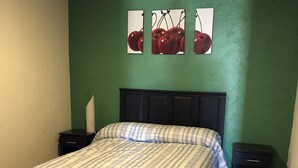 A bedroom with a bed, two bedside tables, a nightstand, and a green wall with three framed pictures. - BEAUTIFUL APARTMENT WITH GREEN TERRACE (Cholula)