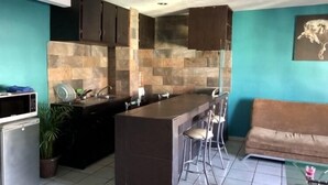A modern kitchen with a central island, two bar stools, a refrigerator, and a dining area with a sofa. - BEAUTIFUL APARTMENT WITH GREEN TERRACE (Cholula)
