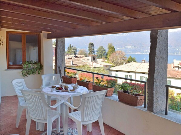 A balcony with a table and chairs, potted plants, and a view of buildings and mountains.