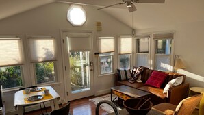 Ein gemütlicher Wohnbereich mit Sofa, Couchtisch und Esstisch. Ein Fenster mit Jalousien, ein Deckenventilator und eine Tür mit Fenster sind ebenfalls vorhanden.