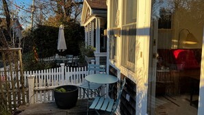 Eine überdachte Terrasse im Freien mit Tisch und Stühlen, ein weißer Zaun und ein großer Pflanzkasten.