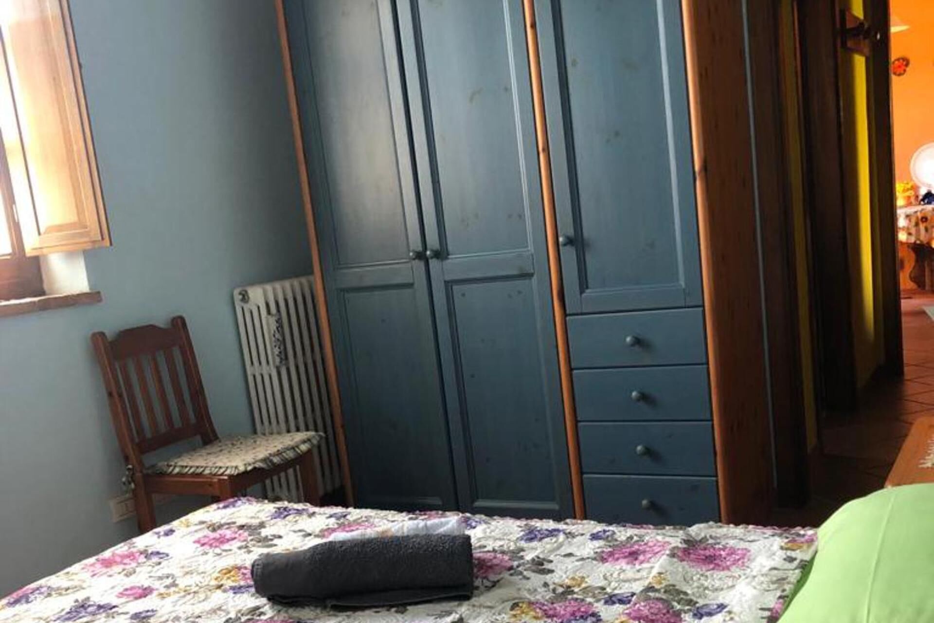 A bedroom with a bed, a chair, a wardrobe, and a radiator.
